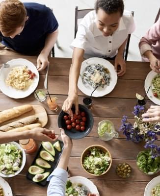 People having dinner at the table ad reaching for tomatos.