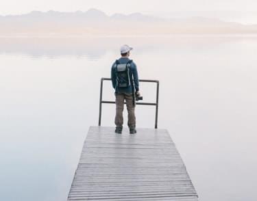 Man with camera standing on the platform over the lake, looking at the landscape.